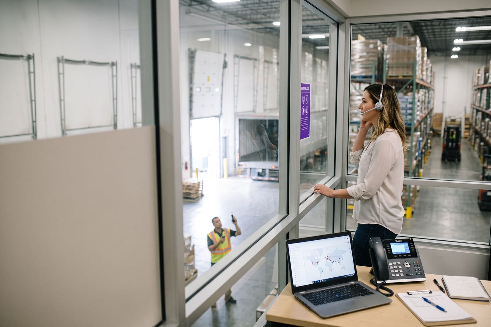 Logistics coordinator with a headset overlooking a warehouse floor