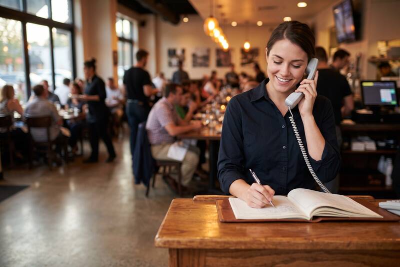 Restaurant host at the host stand talking on a cordless phone